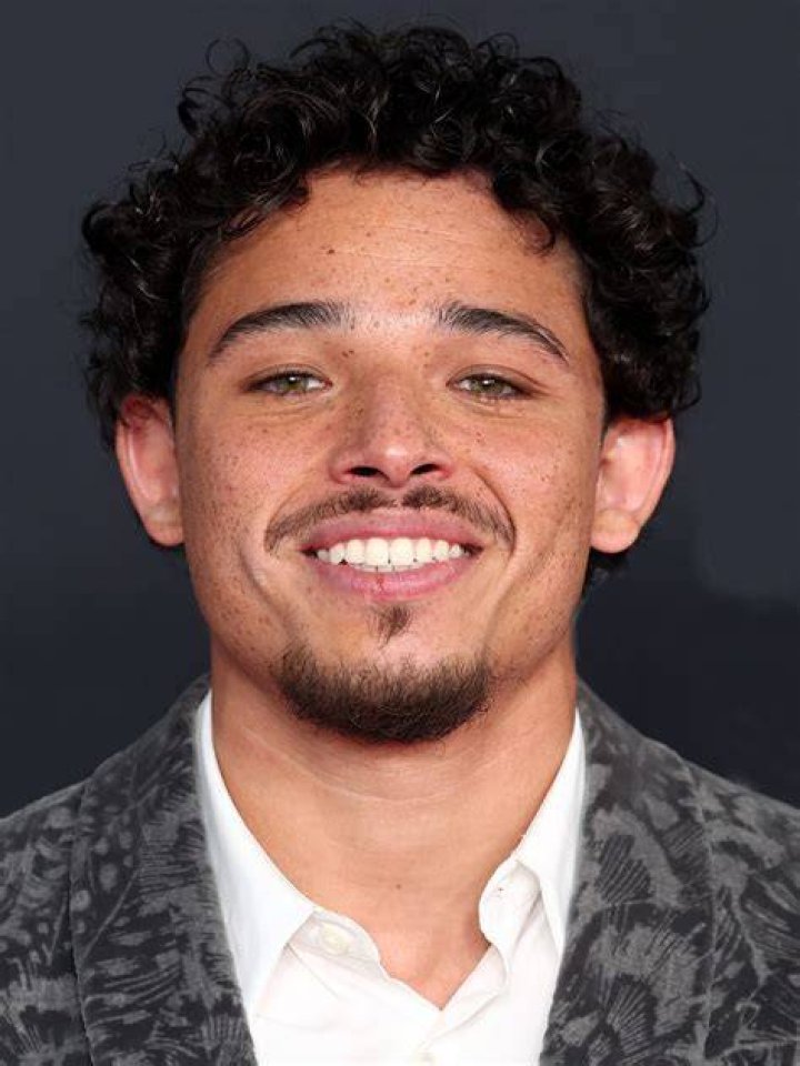 Anthony Ramos smiling in a white t-shirt and white jacket.